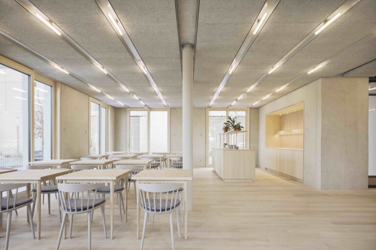 Heller, moderner Gastraum mit mehreren weißen Tischen und Stühlen, großen Fenstern und minimalistischer Einrichtung.