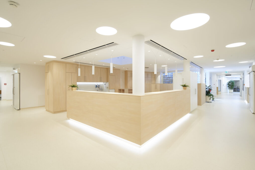 Heller, moderner Empfangsbereich mit hellem Holz, weißen Wänden und Deckenleuchten in einer Klinik.