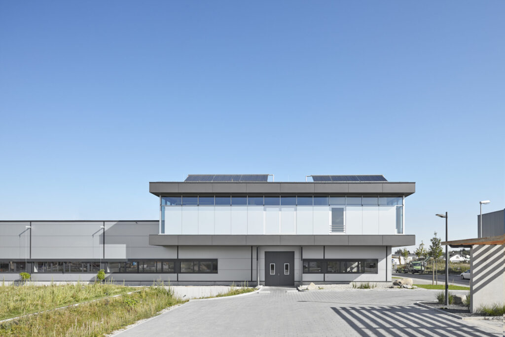 Modernes, zweistöckiges Bürogebäude mit großen Fenstern und Solarpaneelen auf dem Flachdach unter klarem Himmel.