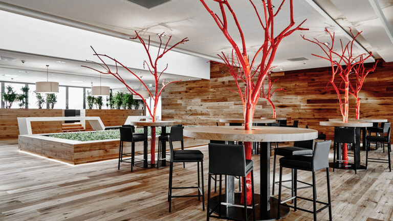 Moderner Gastraum mit runden Tischen, schwarzen Stühlen und roten Baumskulpturen als Dekoration.